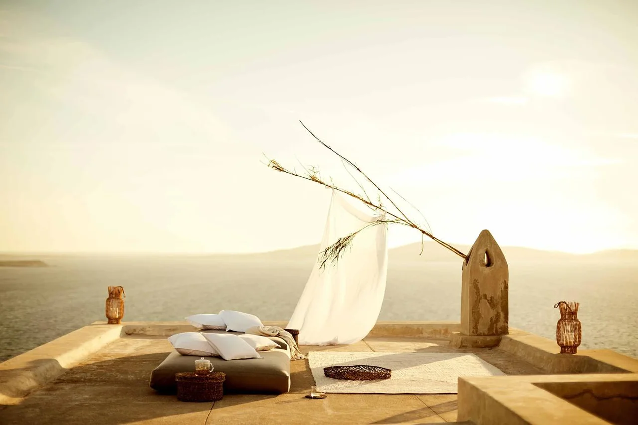 Mediterranean terrace with linen seating, a sculptural vase and sea at golden hour